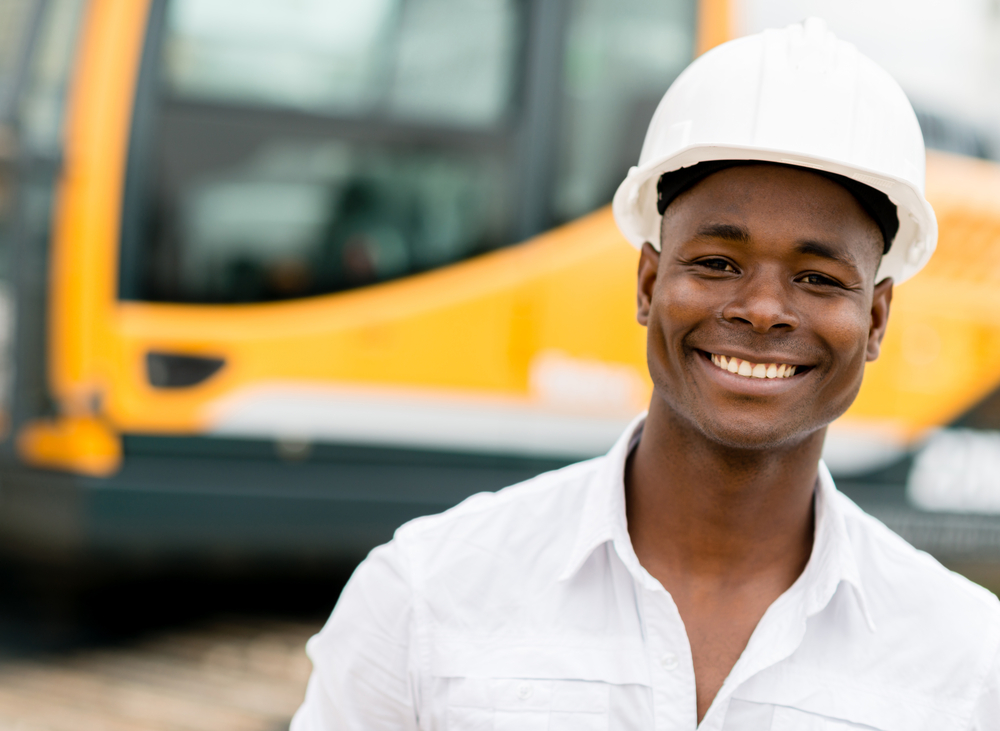 Construction worker with machines at the background looking happy Construction worker with machines at the background looking happy